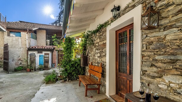 Un patio con un muro de piedra, un banco de madera, una mesa con copas de vino y una puerta con panel de vidrio.