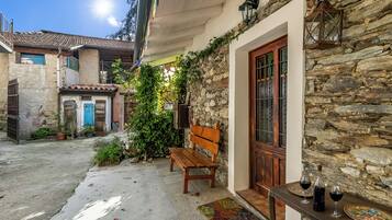A courtyard with a stone wall, a wooden bench, a table with wine glasses, and a door with a glass panel.