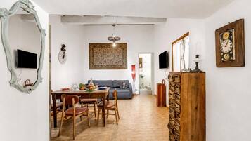 A dining area with a wooden table, chairs, and a television. There is a sofa and a decorative wall piece in the background.