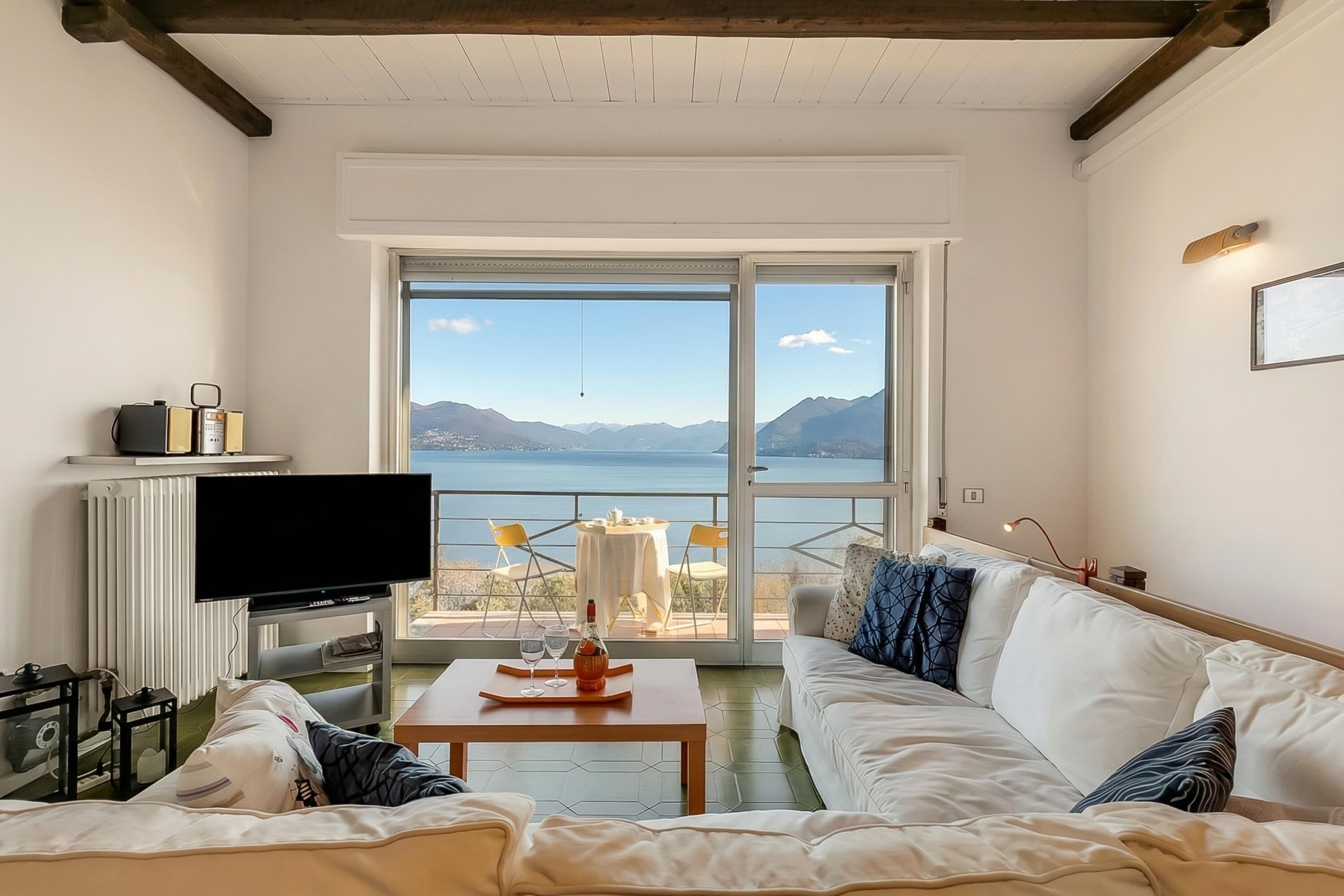 A living room with a sofa, a coffee table, a TV, and a view of the sea.