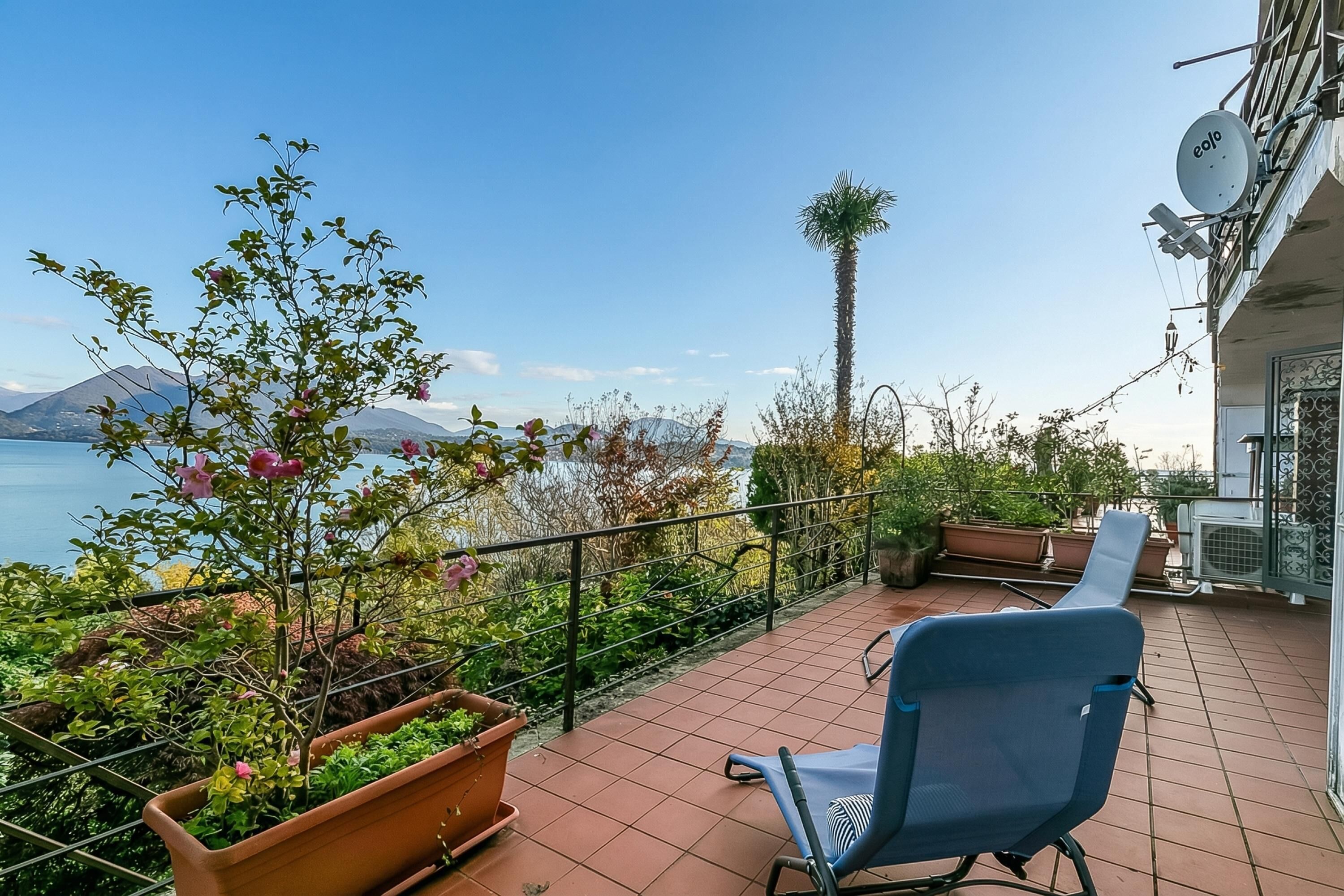 Ein Balkon mit Stuhl, Topfpflanzen und Blick auf Meer und Berge.