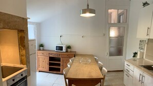 Une cuisine de taille réduite avec une table en bois, des chaises blanches, un four à micro-ondes et un luminaire suspendu.