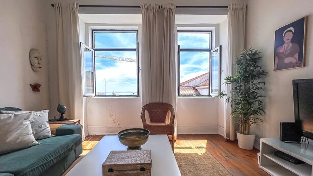 Un salon comprenant un canapé, une table basse avec une boîte décorative, un fauteuil, un téléviseur et une grande fenêtre avec des rideaux.