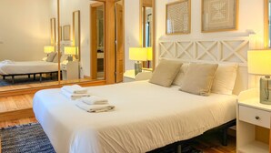 A hotel room with a large bed, bedside tables with lamps, a wardrobe, and two framed artworks on the wall. - Charming 2 Bedroom Apartment w/ River View (Lisboa)