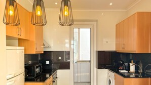 A modern kitchen with wooden cabinets, a black countertop, a stainless steel range, a microwave, a washing machine, and pendant lights. - Charming 2 Bedroom Apartment w/ River View (Lisboa)