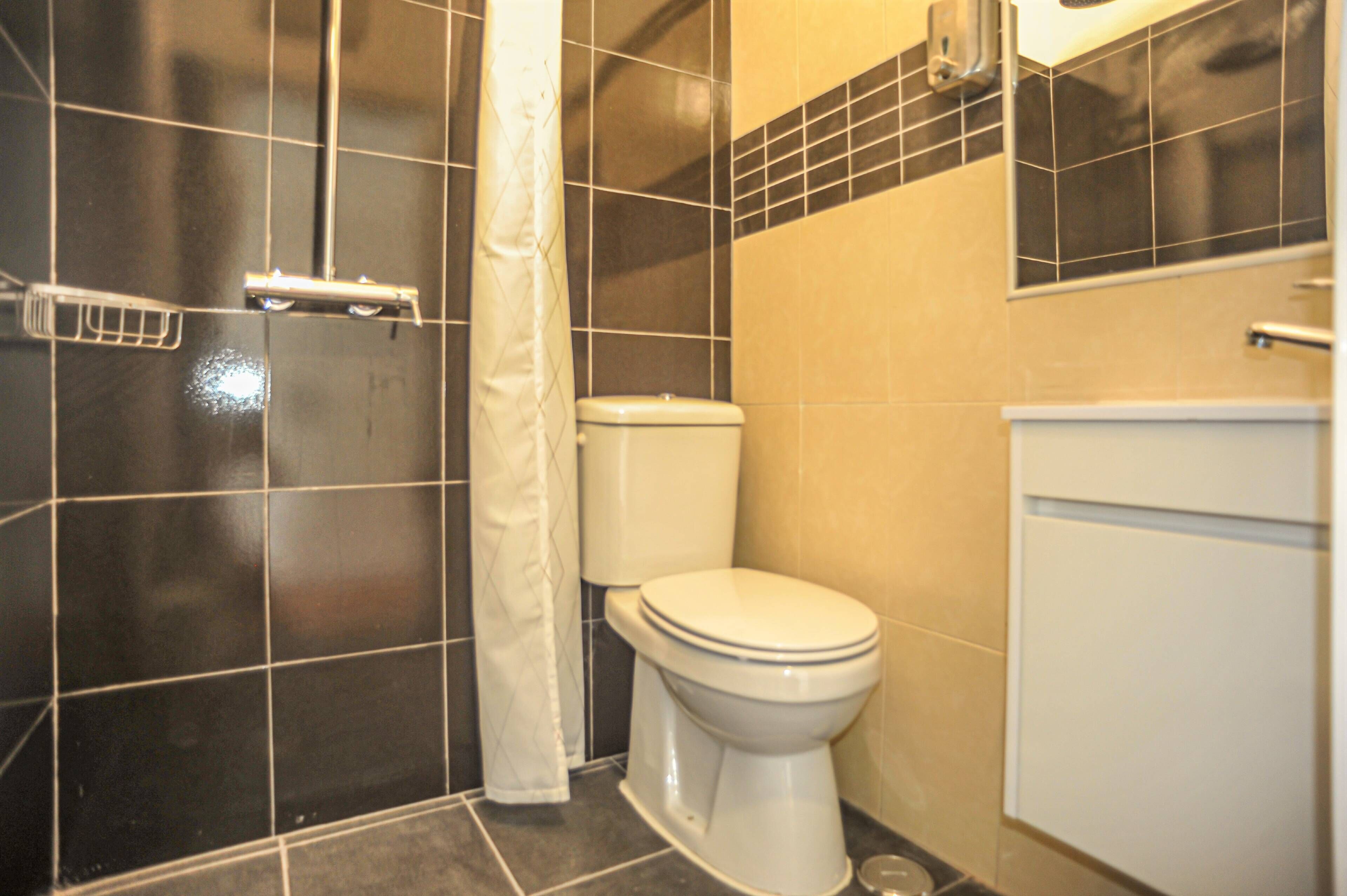 Een badkamer met toilet, douchegordijn en betegelde wanden.
