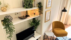 A living room with a flat-screen TV on a white stand, a mustard-colored chair, and shelves with plants and decorative items. - Apartment w/ Balcony in Príncipe Real (Lisboa)