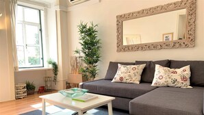 A living room with a grey sofa, a white coffee table, a mirror with an ornate frame, and a large window. - Apartment w/ Balcony in Príncipe Real (Lisboa)