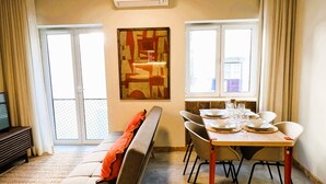 Un salon avec un canapé, une table à manger dressée avec des assiettes et des verres, et un grand tableau abstrait accroché au mur.