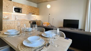 A modern kitchen with a microwave, stove, and sink. There is a dining table set with plates, glasses, and cutlery. A television is mounted on the wall.