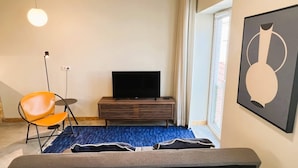 A modern living room with a sofa, a television on a wooden stand, a blue rug, and a framed artwork on the wall.