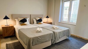 A hotel room with two beds, a window with a view, and a nightstand with a lamp.