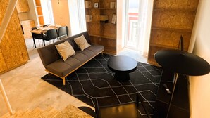 A modern living room with a sofa, a round coffee table, and a dining area with a table and chairs. - NEW Top Modern Loft w/ AC & River View (Lisboa)