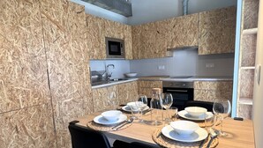 A modern kitchen with wooden walls, a built-in microwave, and a dining area set for four with a table, chairs, and dinnerware. - NEW Top Modern Loft w/ AC & River View (Lisboa)