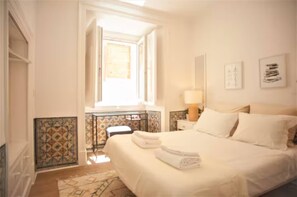 A hotel room with a bed, a nightstand, a lamp, a window, and a view of the outside. - Apartment with Terrace in Príncipe Real (Lisboa)