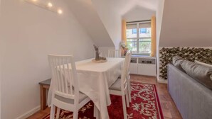 A dining area with a table and chairs, a red patterned rug, a window with curtains, and a sofa with a patterned headboard. - Spacious Loft w/ City view in Principe Real (Lisboa)