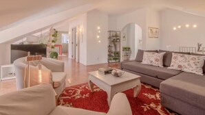 A spacious living room with a high ceiling, a grey sofa set, a white coffee table, and a red patterned rug. There is a TV in the background and a plant on a shelf. - Spacious Loft w/ City view in Principe Real (Lisboa)