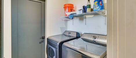A laundry room with two front-loading washing machines, a shelf with cleaning supplies, and a grey door.