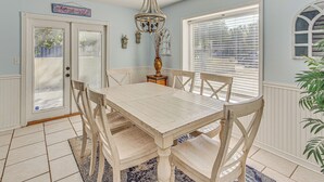 A dining room with a white table and chairs, a chandelier, and a window with blinds.