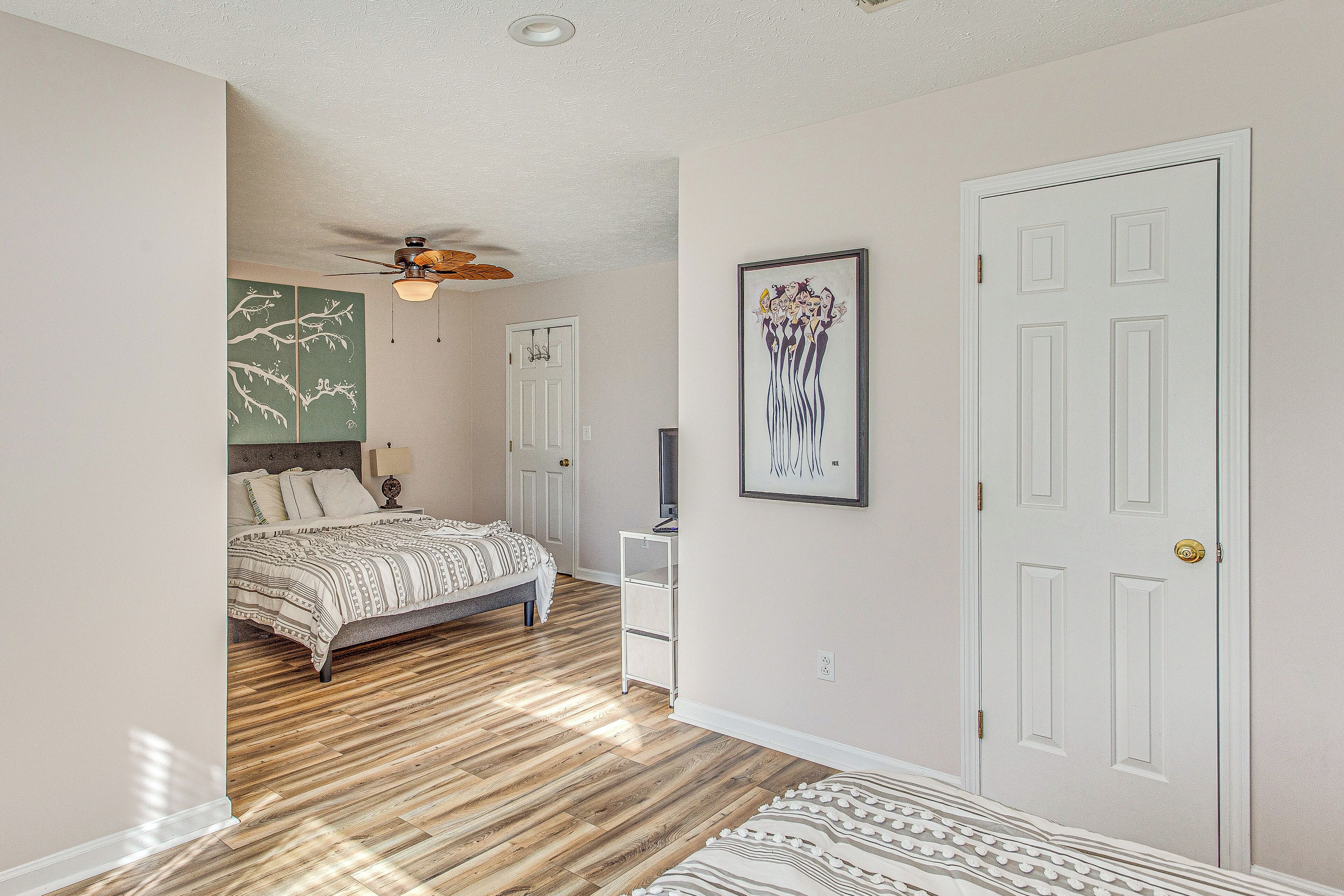 A bedroom with a bed, a ceiling fan, a white door, and a framed picture on the wall.