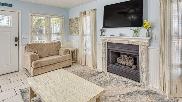 A living room with a beige sofa, a wooden coffee table, a fireplace, a flat-screen TV, and a ceiling fan.