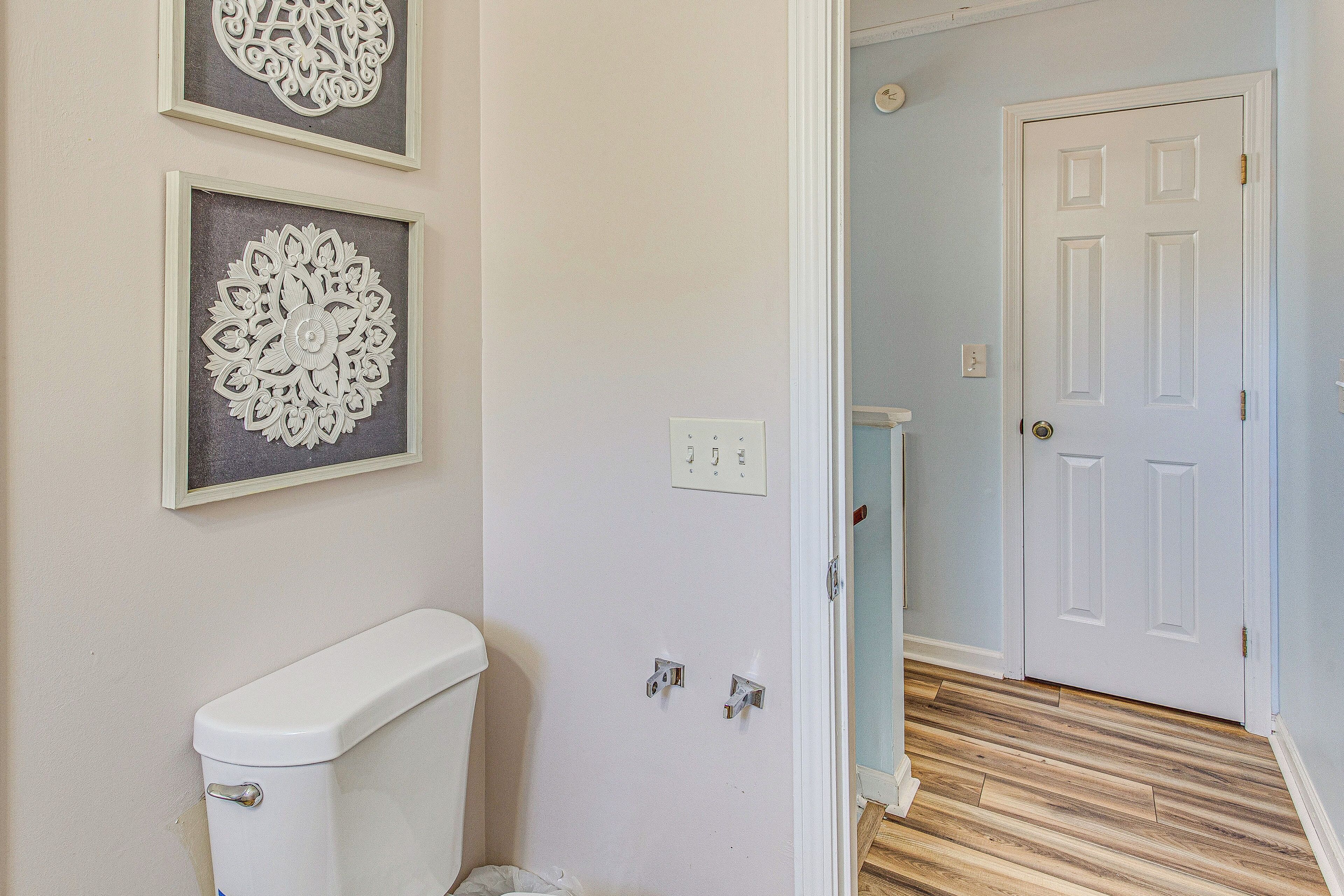 Une salle de bain avec des toilettes, deux éléments de décoration encadrés accrochés au mur, et une porte blanche donnant sur une autre pièce.