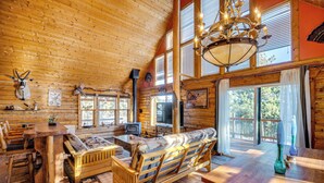 A log cabin interior with a wooden dining table, sofa, and a television. - 4 Mi to Fossil Beds: Private Log Cabin on 3 Acres (Florissant)