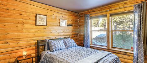 Quarto de cabana de madeira com uma cama, mesa de cabeceira e janela com cortinas.