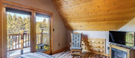 A bedroom with a wooden ceiling, a bed, a television, and a fireplace.