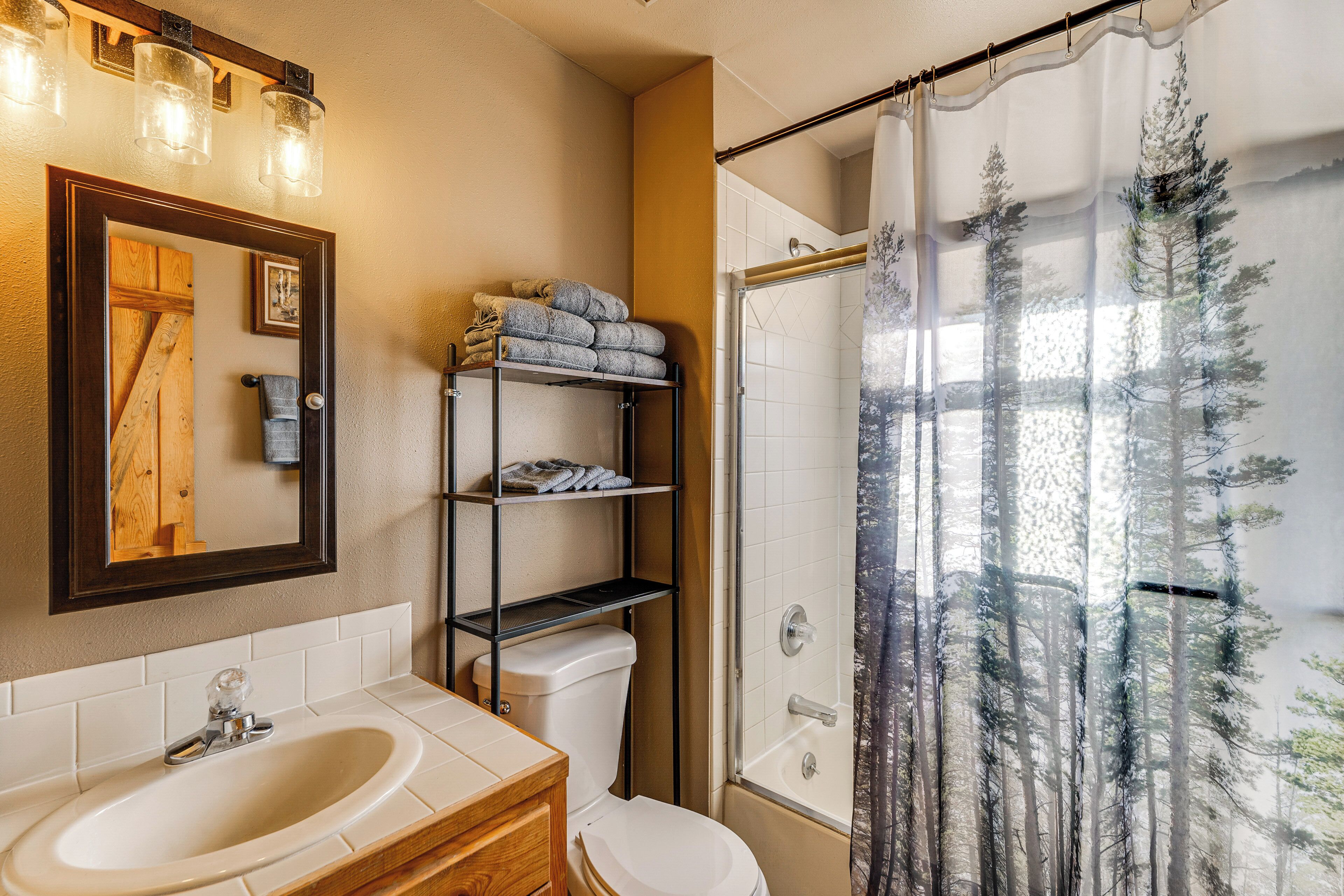 Une salle de bain équipée d’un lavabo, de toilettes et d’un rideau de douche orné d’un motif de forêt.