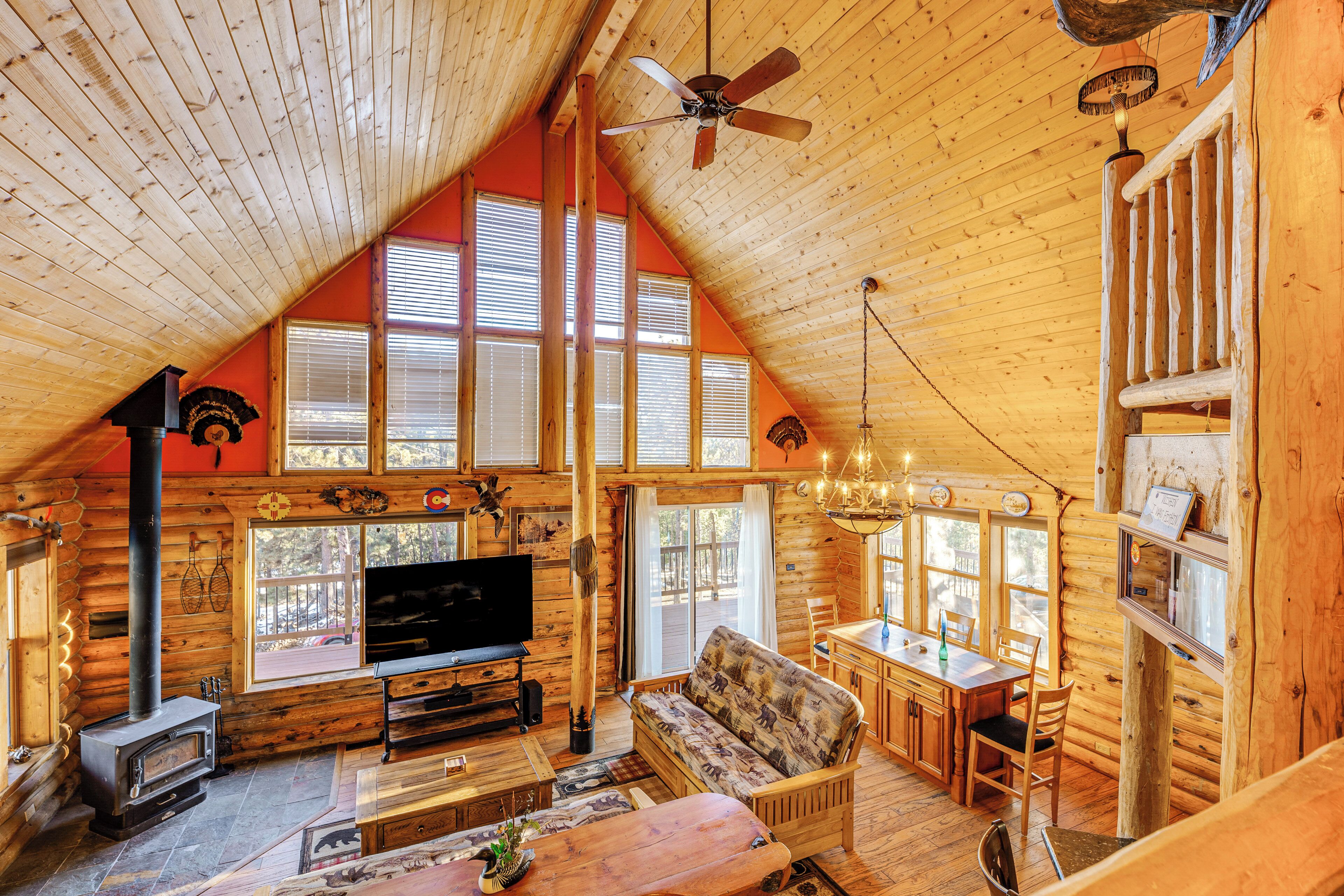 L’intérieur d’une cabane en rondins, avec une cheminée, des meubles en bois, un ventilateur de plafond et de grandes fenêtres.