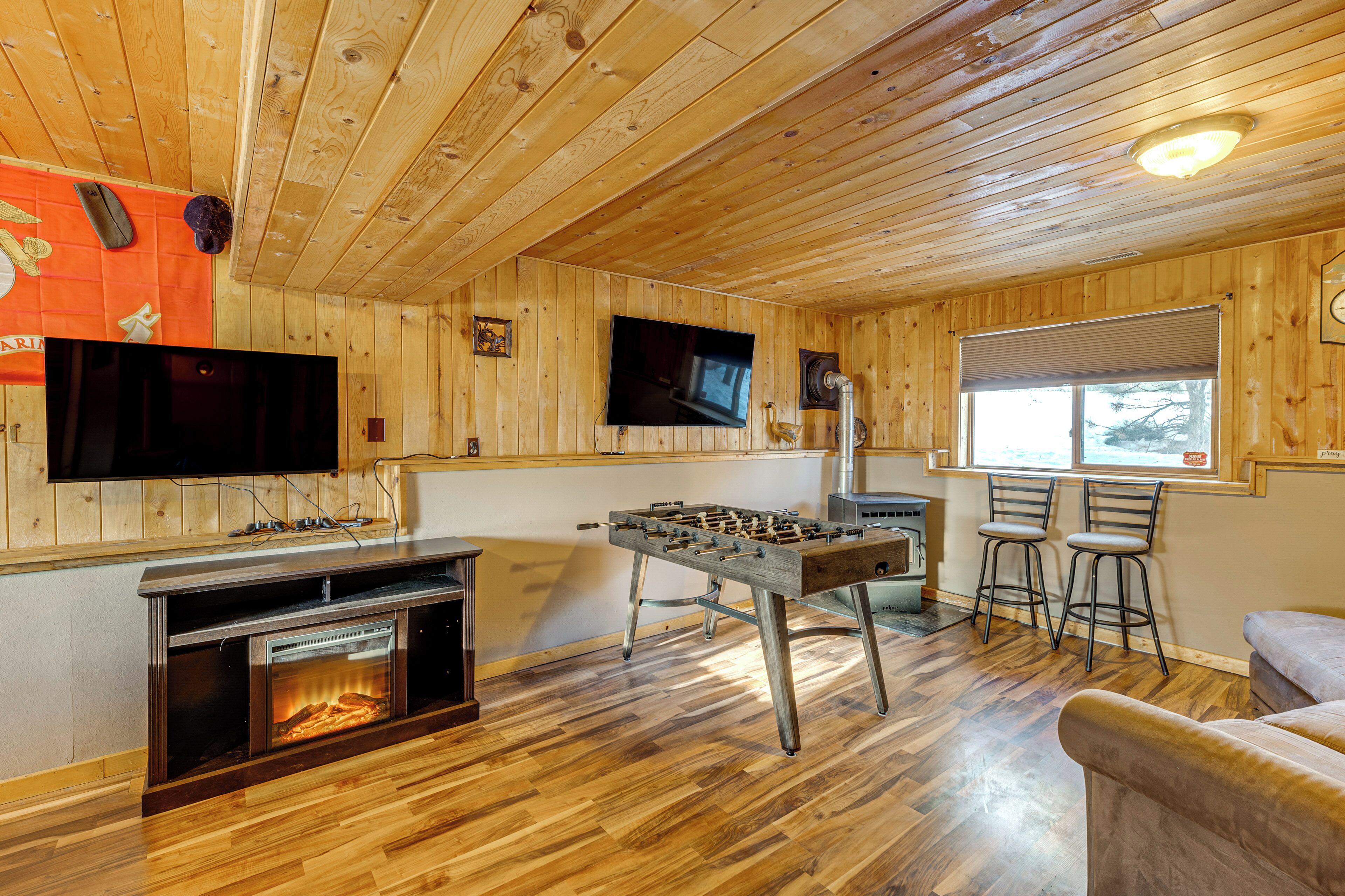 Ein Zimmer mit Holzboden, einer Kicker-Tischfußballmaschine, einem Kamin, einem Fernseher und zwei Barhocker.