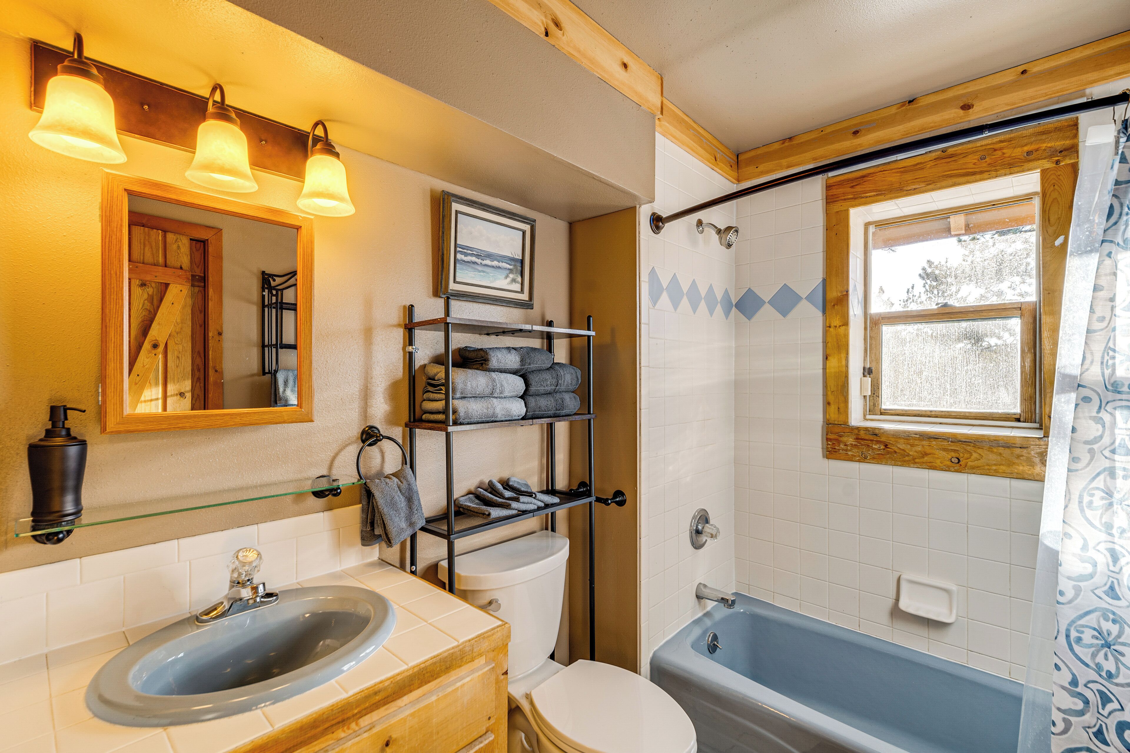 Une salle de bain avec un lavabo, des toilettes et une baignoire. On y trouve une étagère avec des serviettes et un tableau encadré accroché au mur.