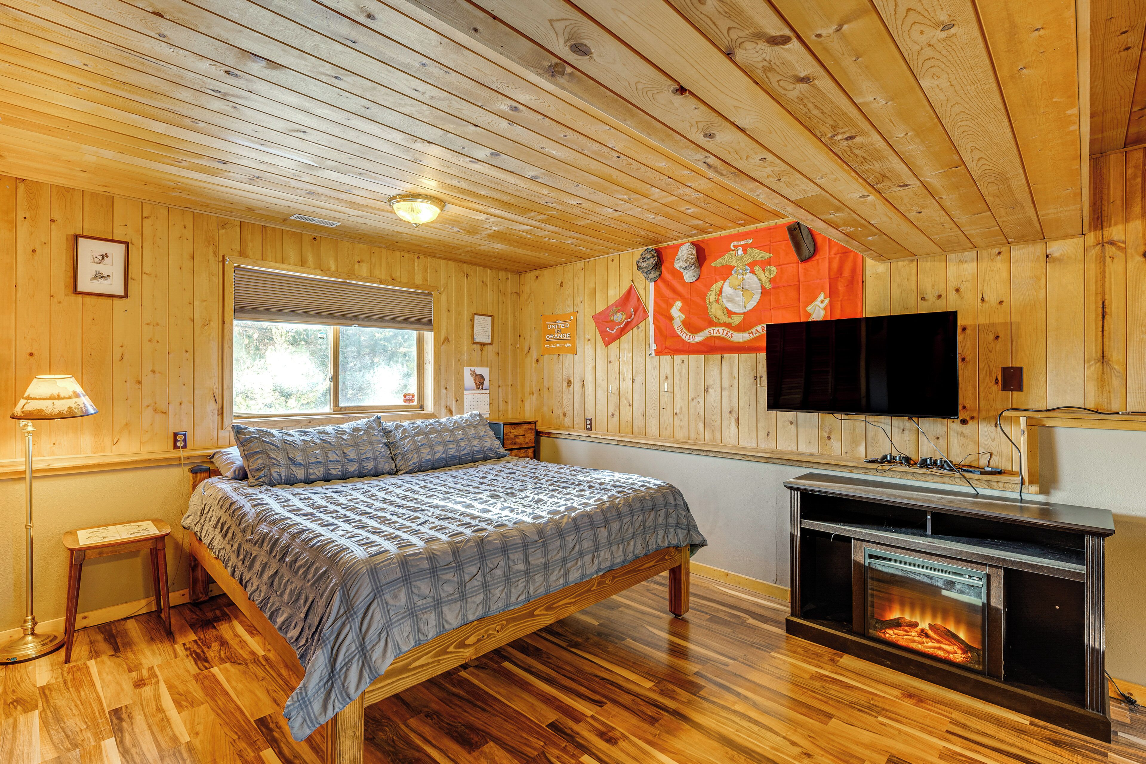 A wooden-paneled room with a bed, a fireplace, a television, and a window.