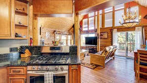 A spacious kitchen with a large stove, wooden cabinets, and a dining area with a TV and comfortable seating. - 4 Mi to Fossil Beds: Private Log Cabin on 3 Acres (Florissant)