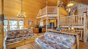 A log cabin interior with a loft bedroom, a dining area, and a living room with two sofas and a fireplace. - 4 Mi to Fossil Beds: Private Log Cabin on 3 Acres (Florissant)