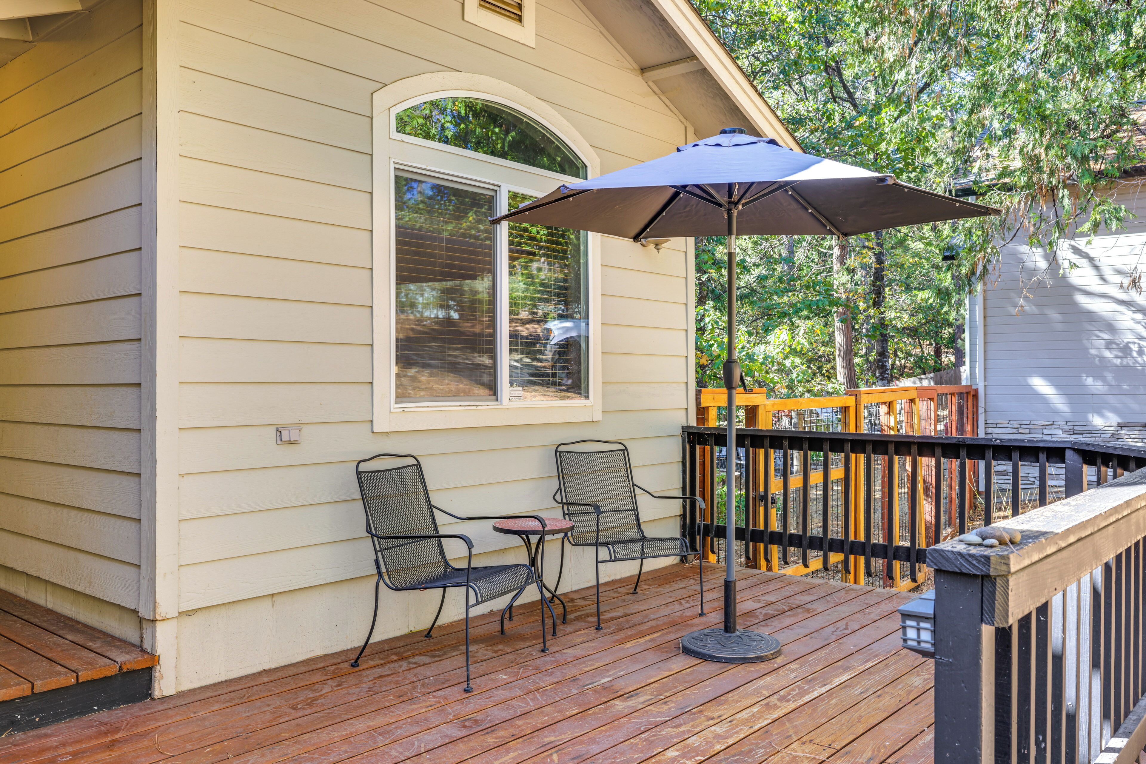A wooden deck with two chairs and a table, a patio umbrella, and a view of a house with a window and a deck railing.