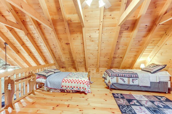 Une chambre mansardée chaleureuse, avec deux lits, des poutres apparentes et un plancher en bois.