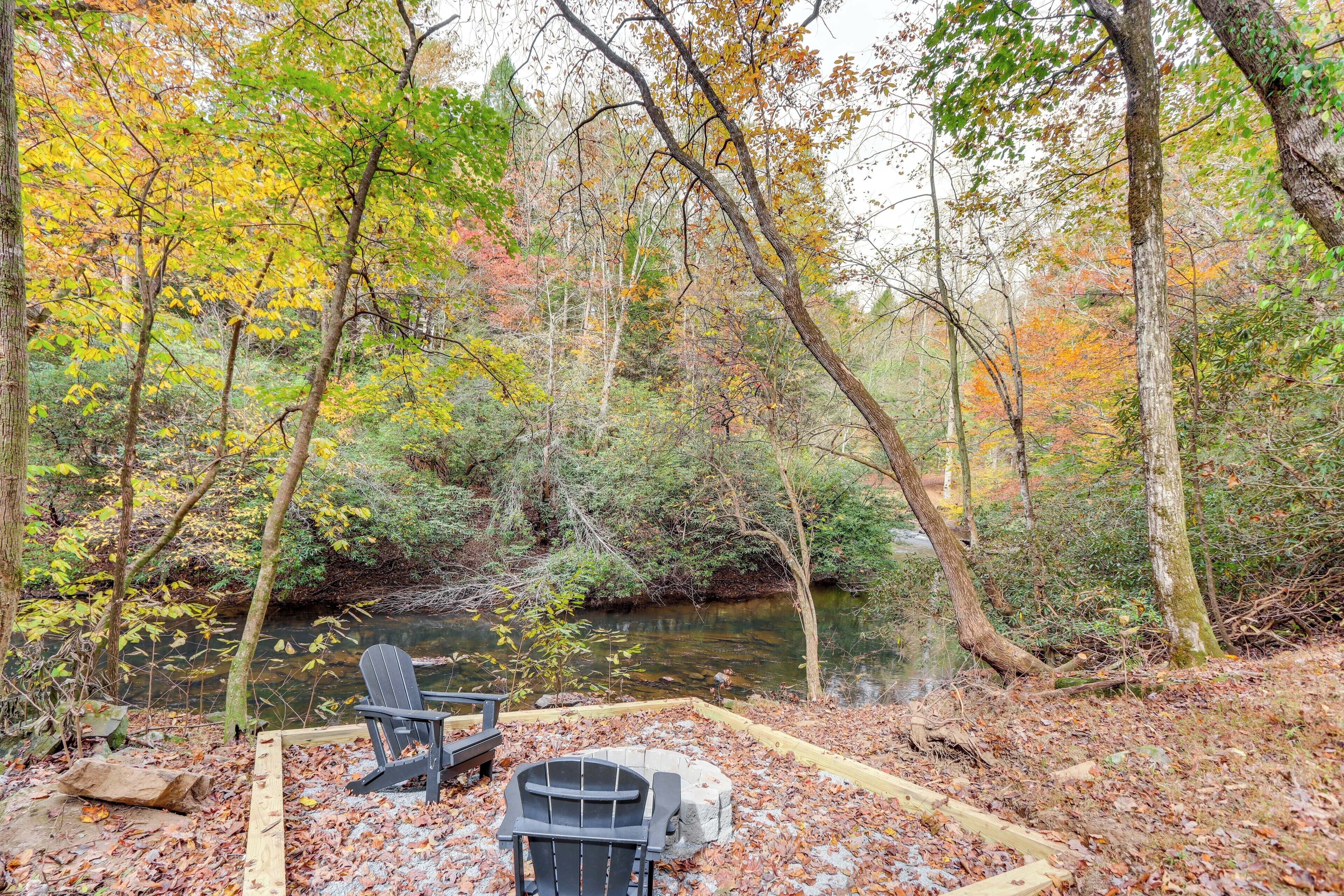 A campsite with a chair and a grill by a river surrounded by trees.