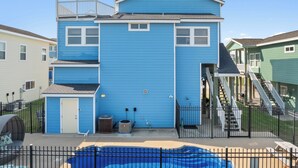 Una casa blu a due piani con un cortile recintato, un piccolo deposito e una piscina.