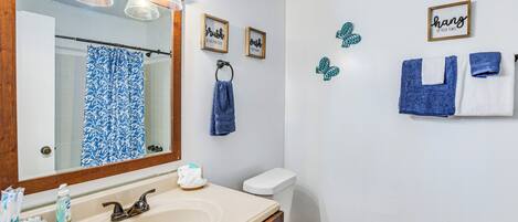 Baño con lavamanos, espejo e inodoro. Hay toallas y adornos en la pared.