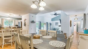 Un vaste espace dédié à la salle à manger, avec une table et des chaises en bois, un ventilateur de plafond et une vue sur le salon.