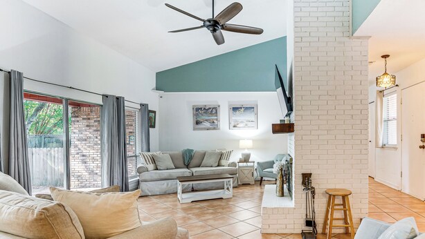 Un salon spacieux avec un grand canapé, une table basse et un ventilateur de plafond. On aperçoit un mur en briques et un mur en briques peintes en blanc à l’arrière-plan.