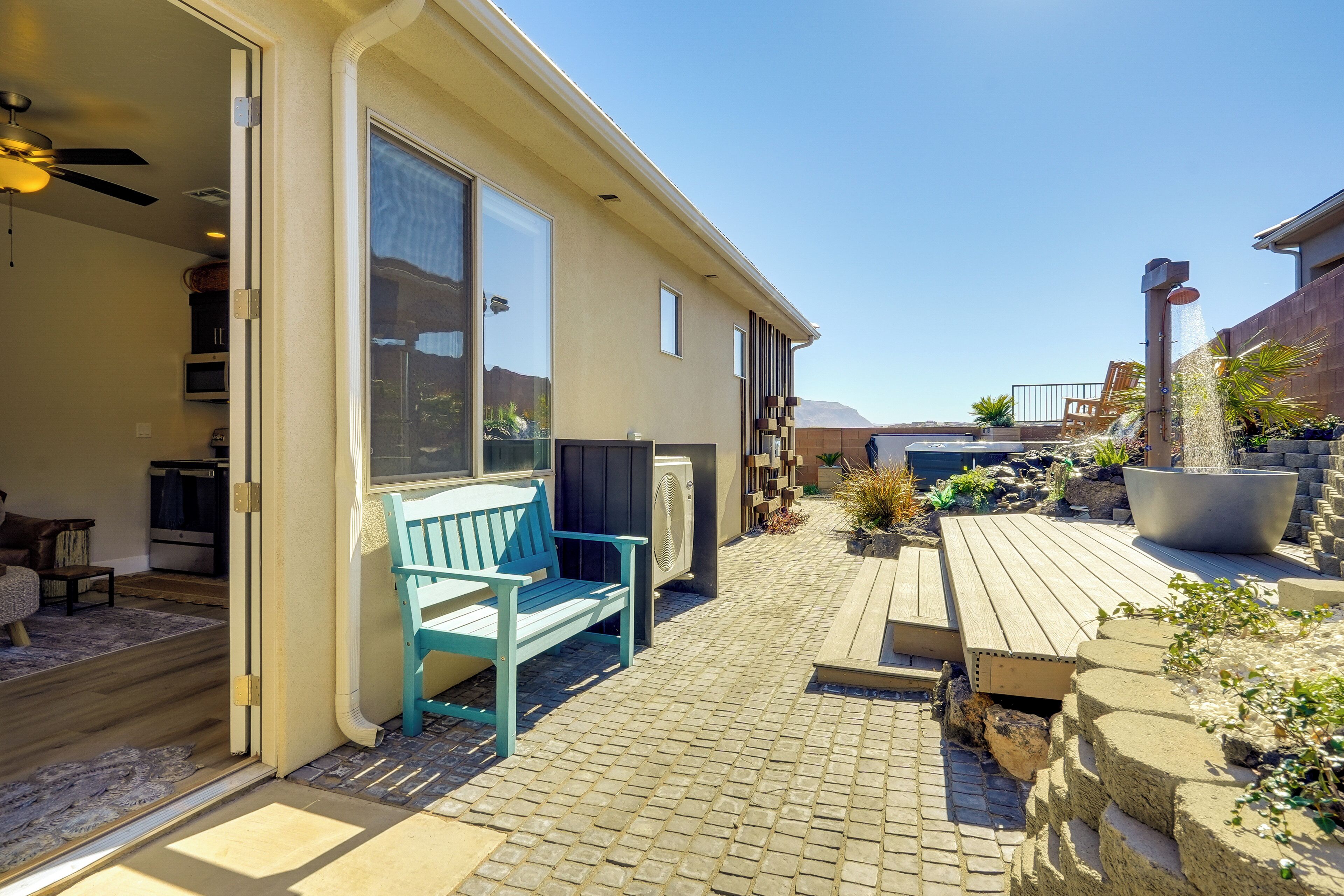 Un espace patio avec une terrasse en bois, un banc bleu et un grand bac à fleurs.