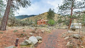 Un rustico chalet con un vialetto sterrato, circondato da pini e rocce.