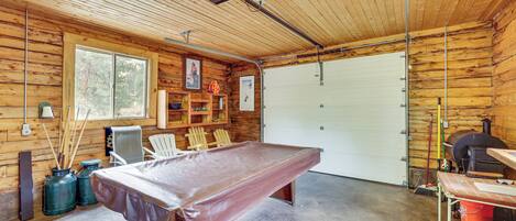 A spacious indoor area with a pool table, wooden walls, a garage door, and various sports equipment.