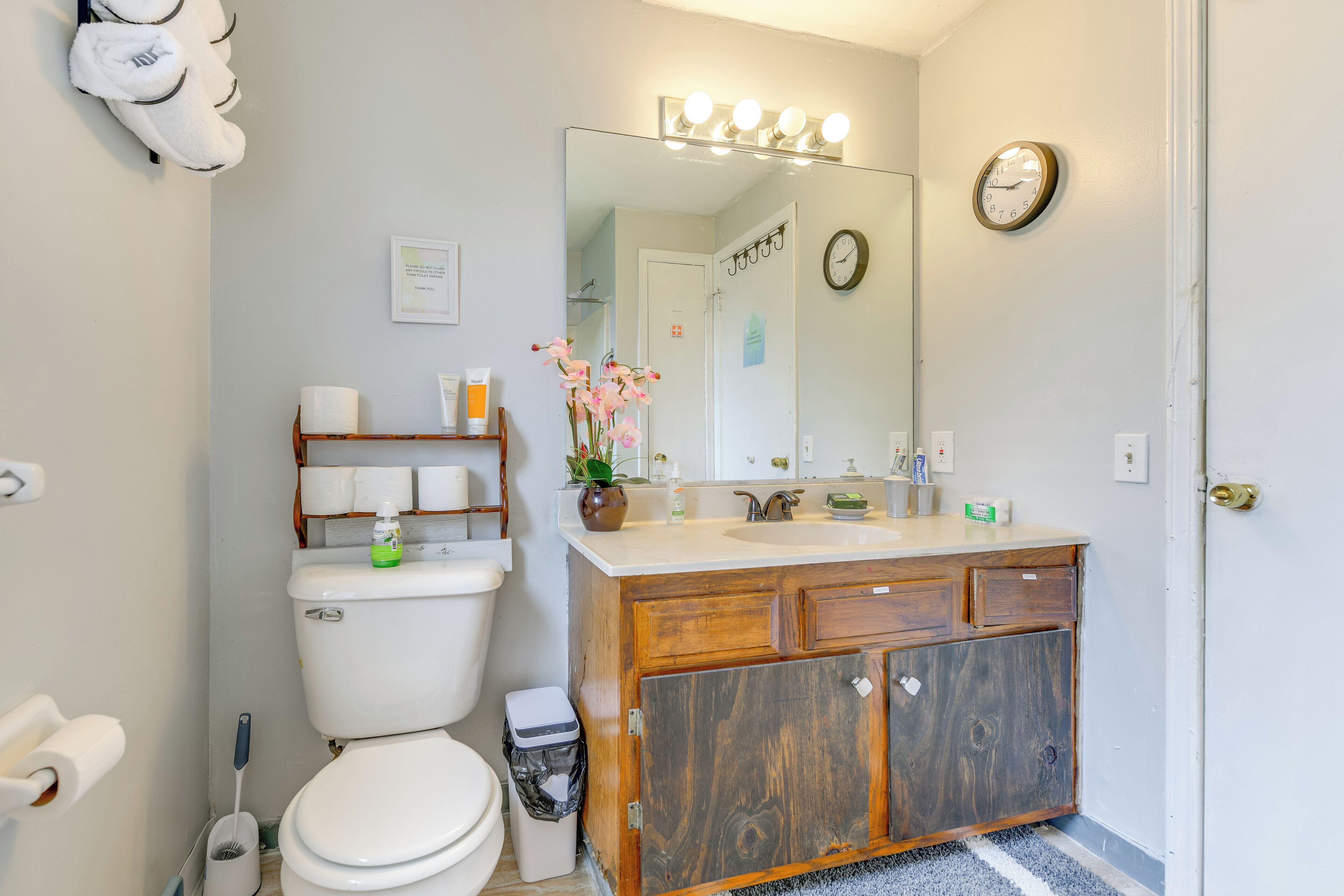 A bathroom with a toilet, sink, vanity, and a mirror with lights.