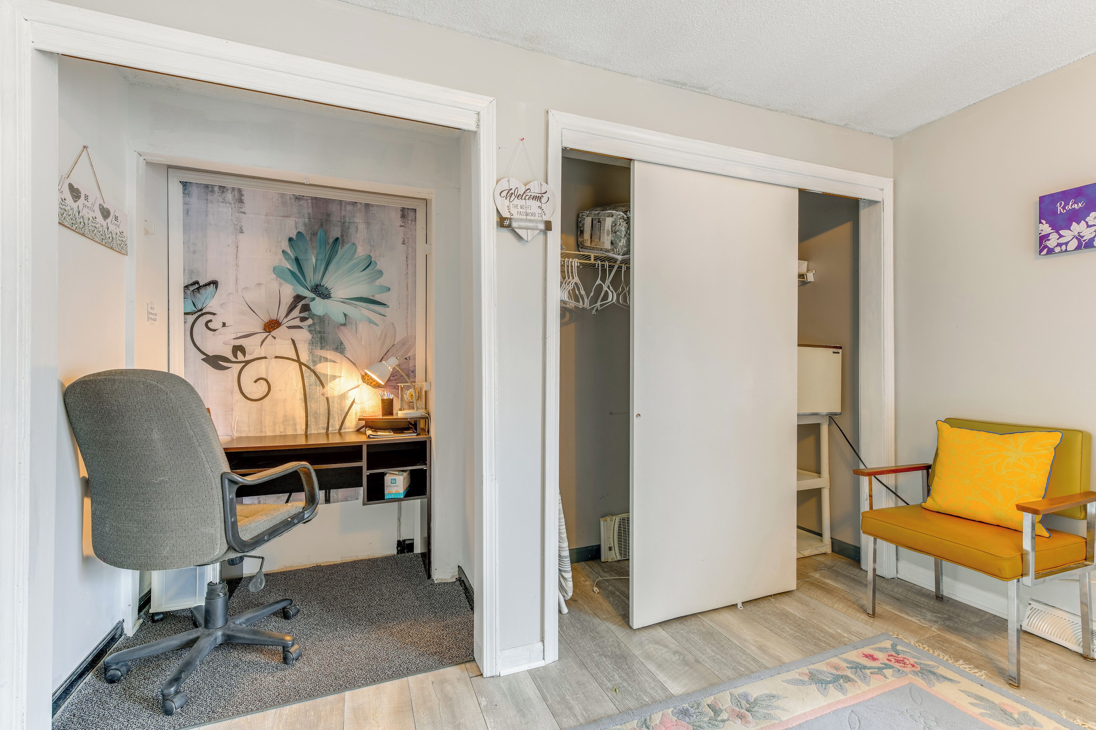 Una habitación con un escritorio, una silla de oficina y un sillón con cojín. Se ve una puerta que da a otra estancia.