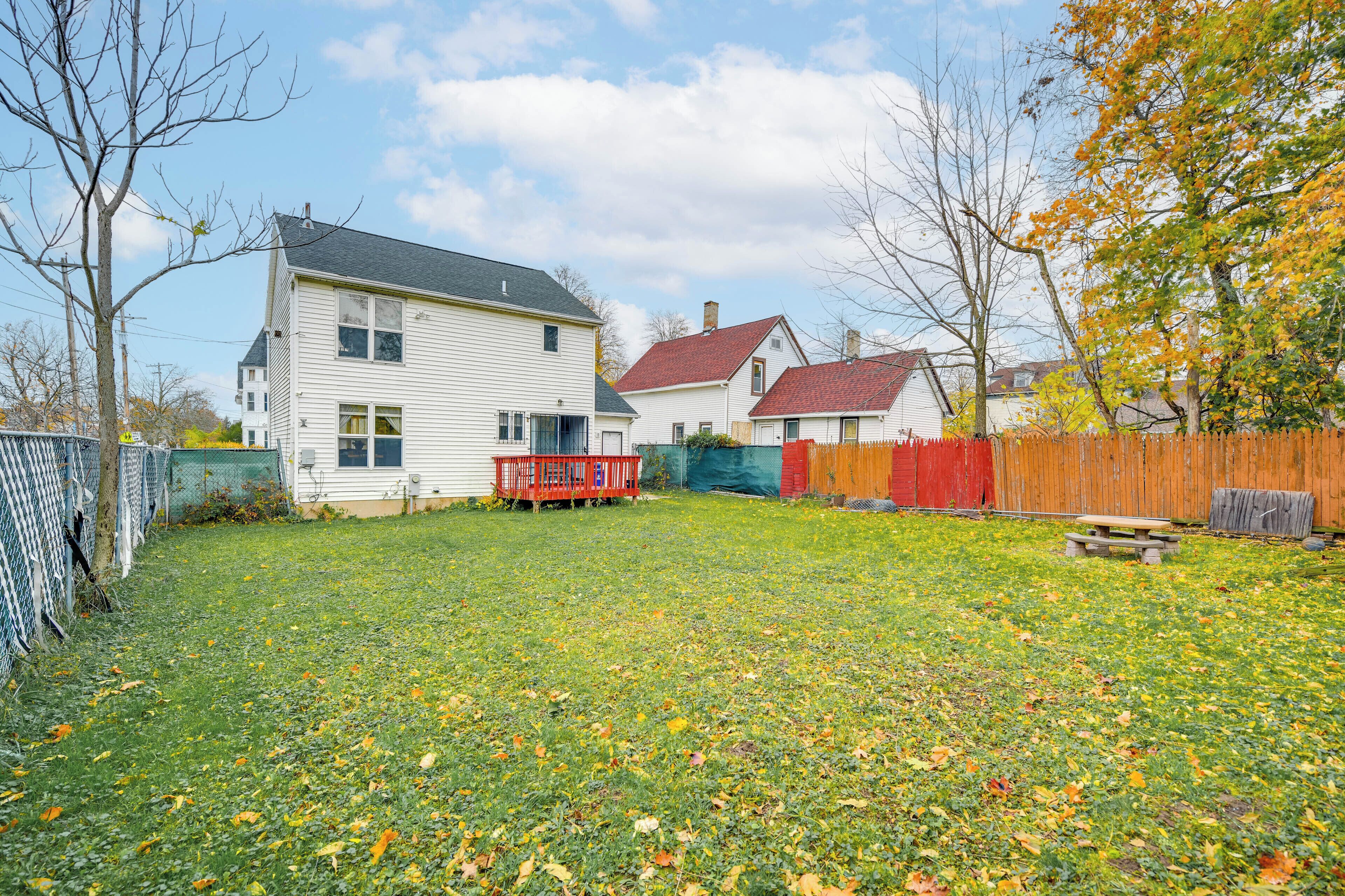 Un jardin à l’arrière d’une maison, avec une clôture en bois et un banc rouge.