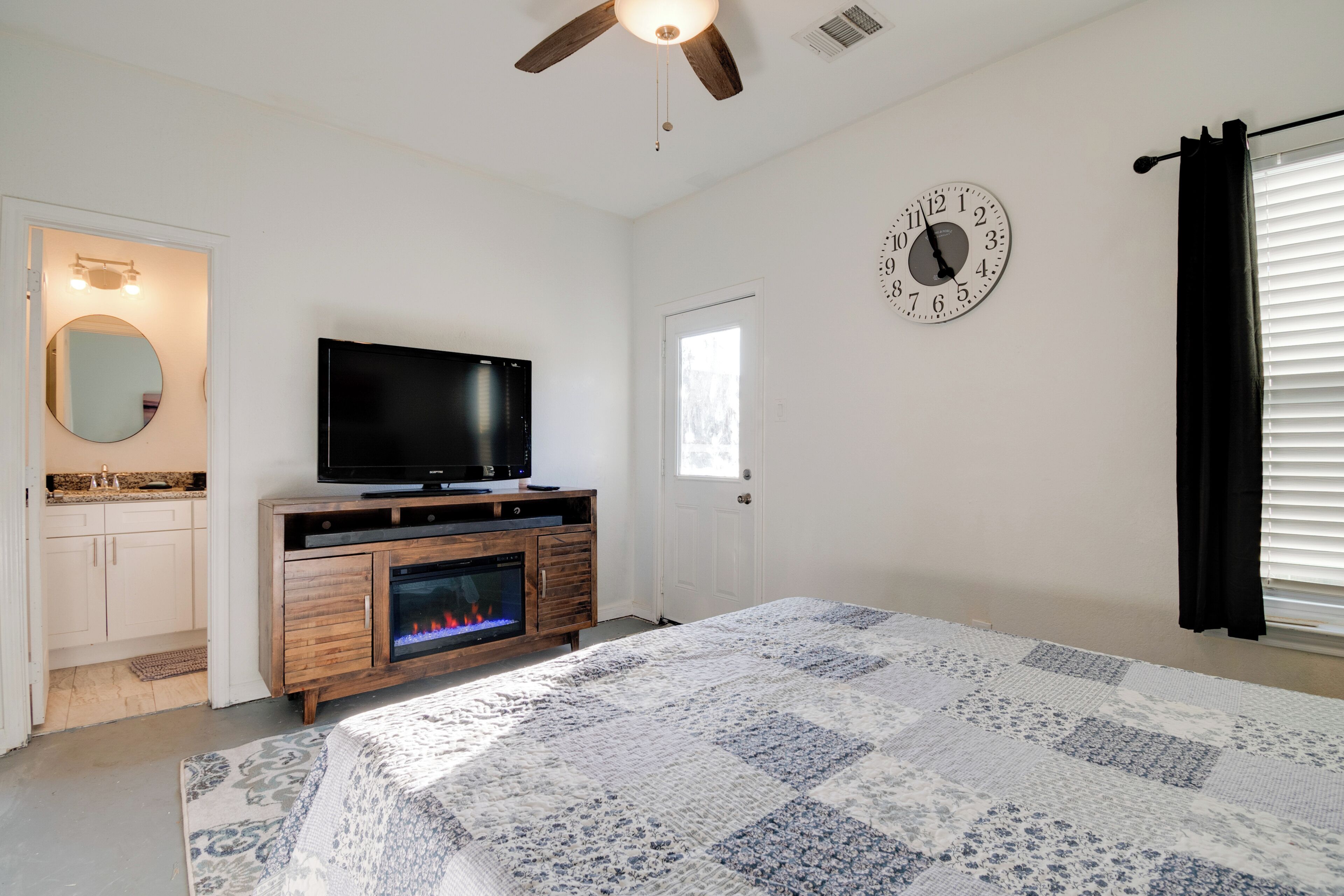 A bedroom with a bed, a television, a fireplace, a clock, and a window with blinds.